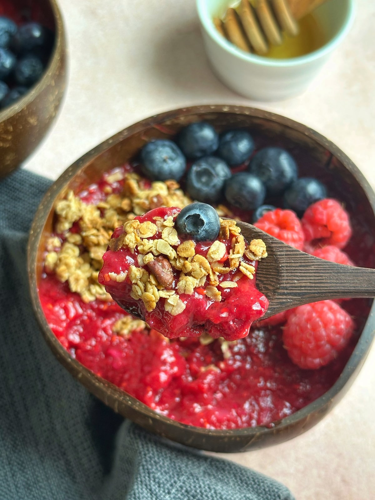 A wooden spoon filled with a bite of a raspberry smoothie bowl.