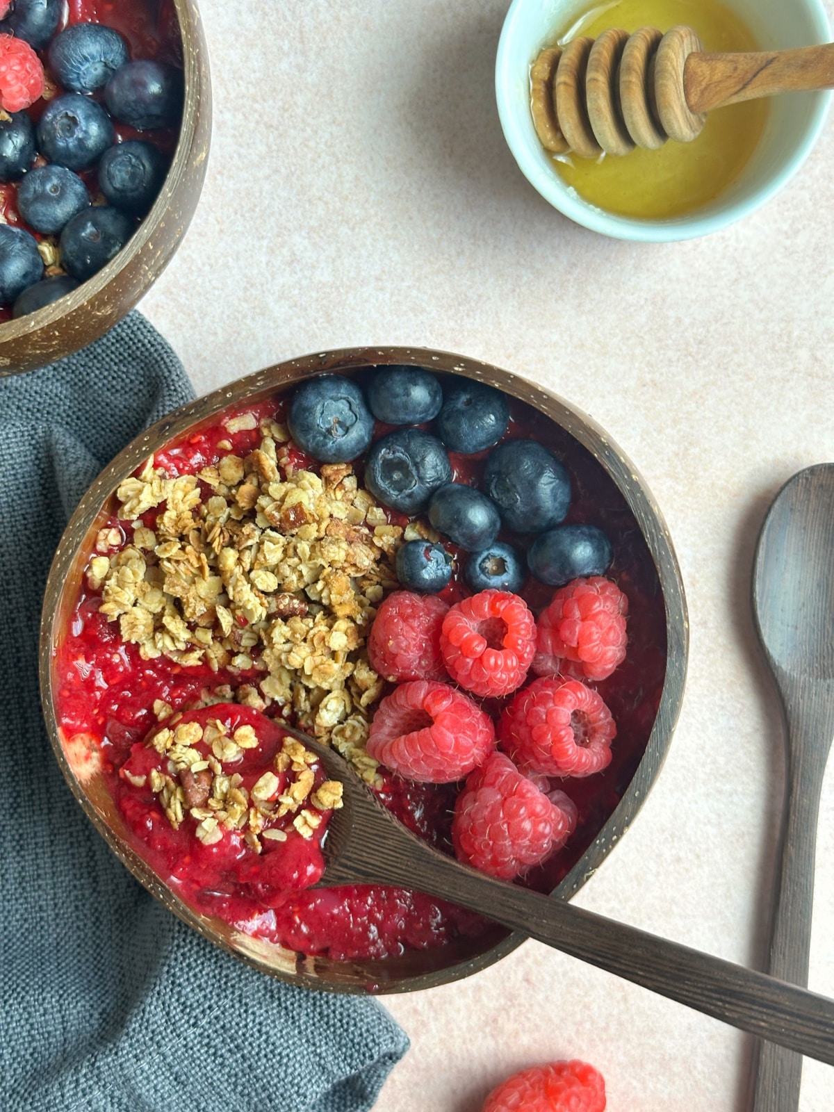 A raspberry smoothie bowl topped with granola and berries, with a spoon stuck in the middle.
