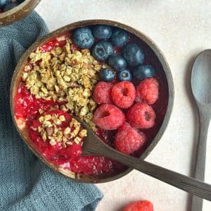A coconut bowl filled with raspberry smoothie, topped with fresh berries and granola.