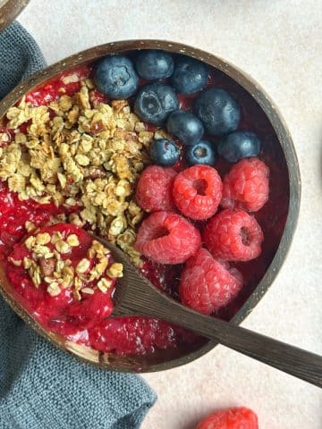 A coconut bowl filled with raspberry smoothie, topped with fresh berries and granola.