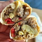Two halved Southwest Chicken Sausage, Egg, & Cheese Breakfast Burritos being held by a hand.