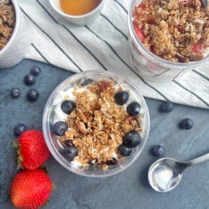 An overhead shot of Greek Yogurt Parfaits with blueberries, granola, and strawberries layered in a clear container.