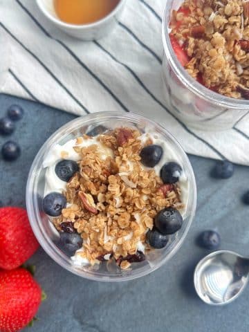 An overhead shot of Greek Yogurt Parfaits with blueberries, granola, and strawberries layered in a clear container.