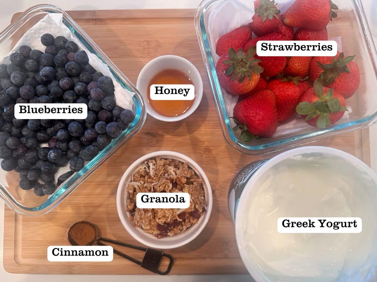 A wooden board containing greek yogurt, berries, honey, and granola.