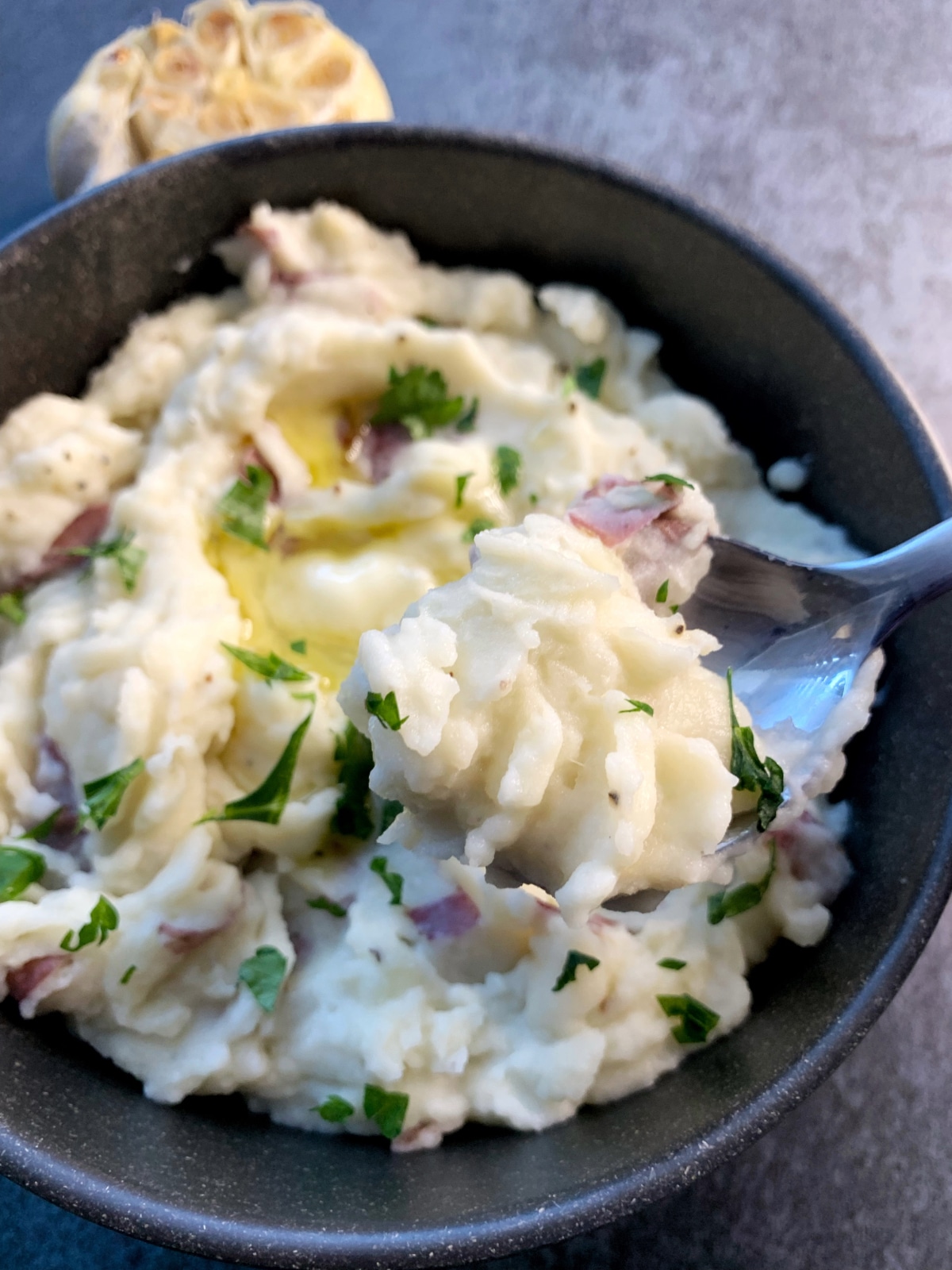 A spoon scooping u a bite of mashed red potatoes with roasted garlic and butter.