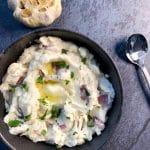 Roasted garlic red skin mashed potatoes in a black bowl with a head of roasted garlic on the side.