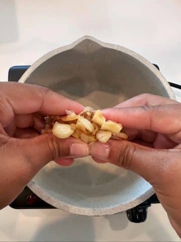 A hand squeezing a head of roasted garlic.