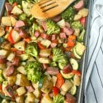 A big pan of Sheet Pan Sausage and Veggies with a white and black striped towel to the side.