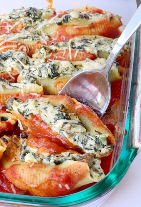 A pan of vegetarian stuffed shells with a spoon sticking out of the marinara sauce.