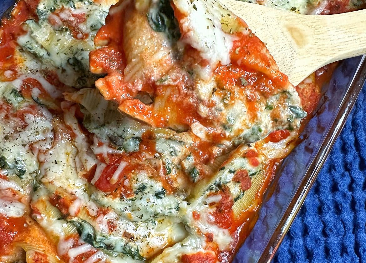A pan of spinach & mushroom vegetarian stuffed shells with a portion scooped out.