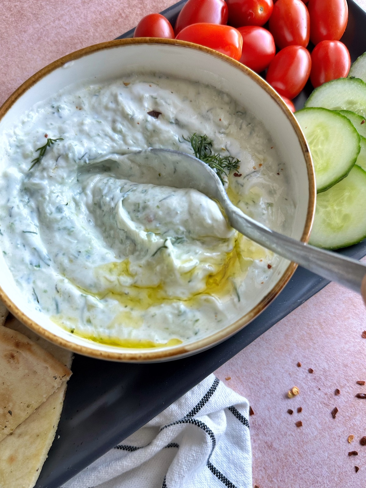 A spoon stirring through a bowl of homemade tzatziki sauce.