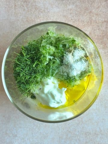 A bowl filled with yogurt, grated cucumber, and fresh herbs.
