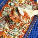 A pan of spinach & mushroom vegetarian stuffed shells with a portion scooped out on a wooden spoon.