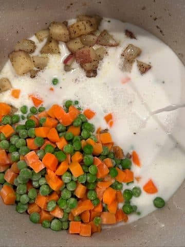 A pot filled with cream, potatoes, and carrots and peas.