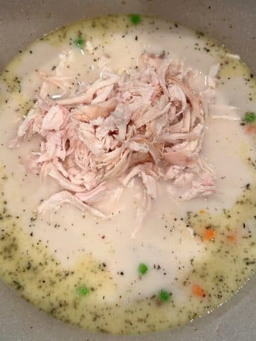 Shredded chicken in the middle of a pot of creamy soup.