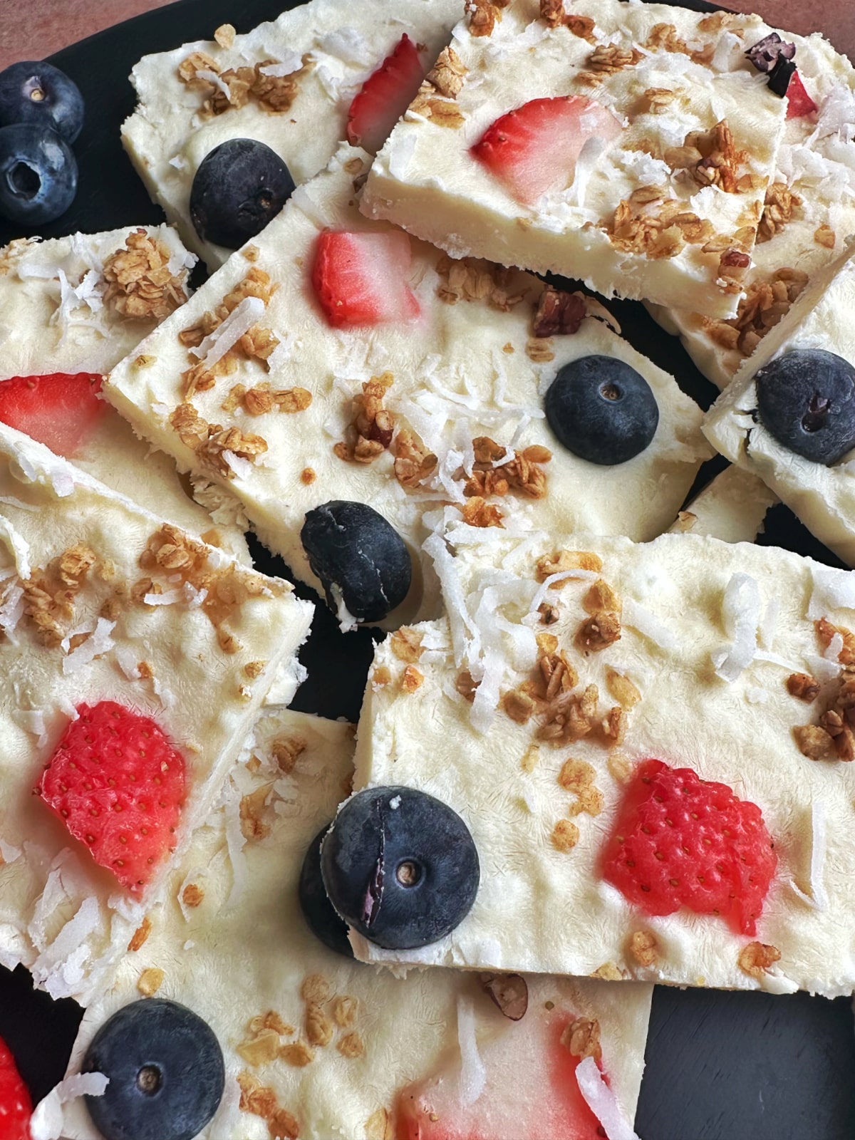 A closeup shot of a stack of yogurt bark squares with berries and granola sprinkled on top.