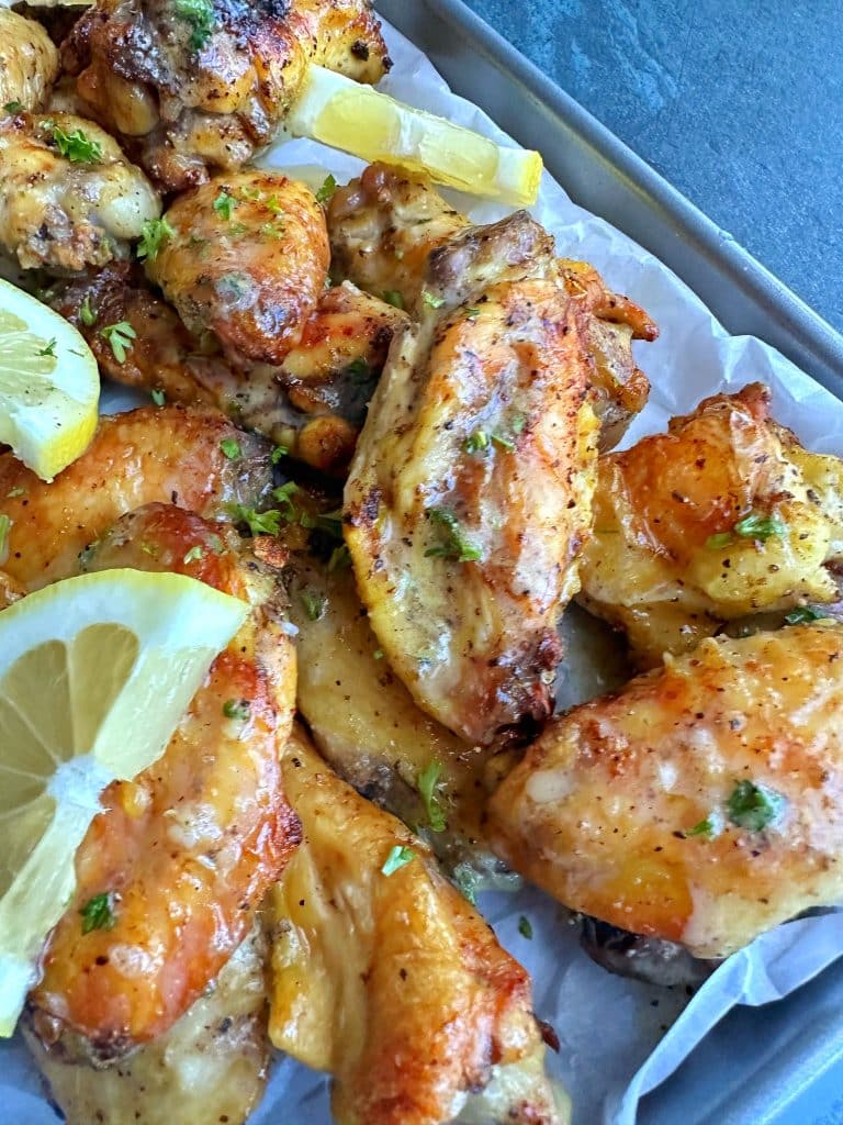 A tray of lemon pepper wet wings with lemon slices and chopped parsley.