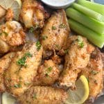 A tray of lemon pepper wet wings with lemon slices, celery sticks, and ranch dressing.