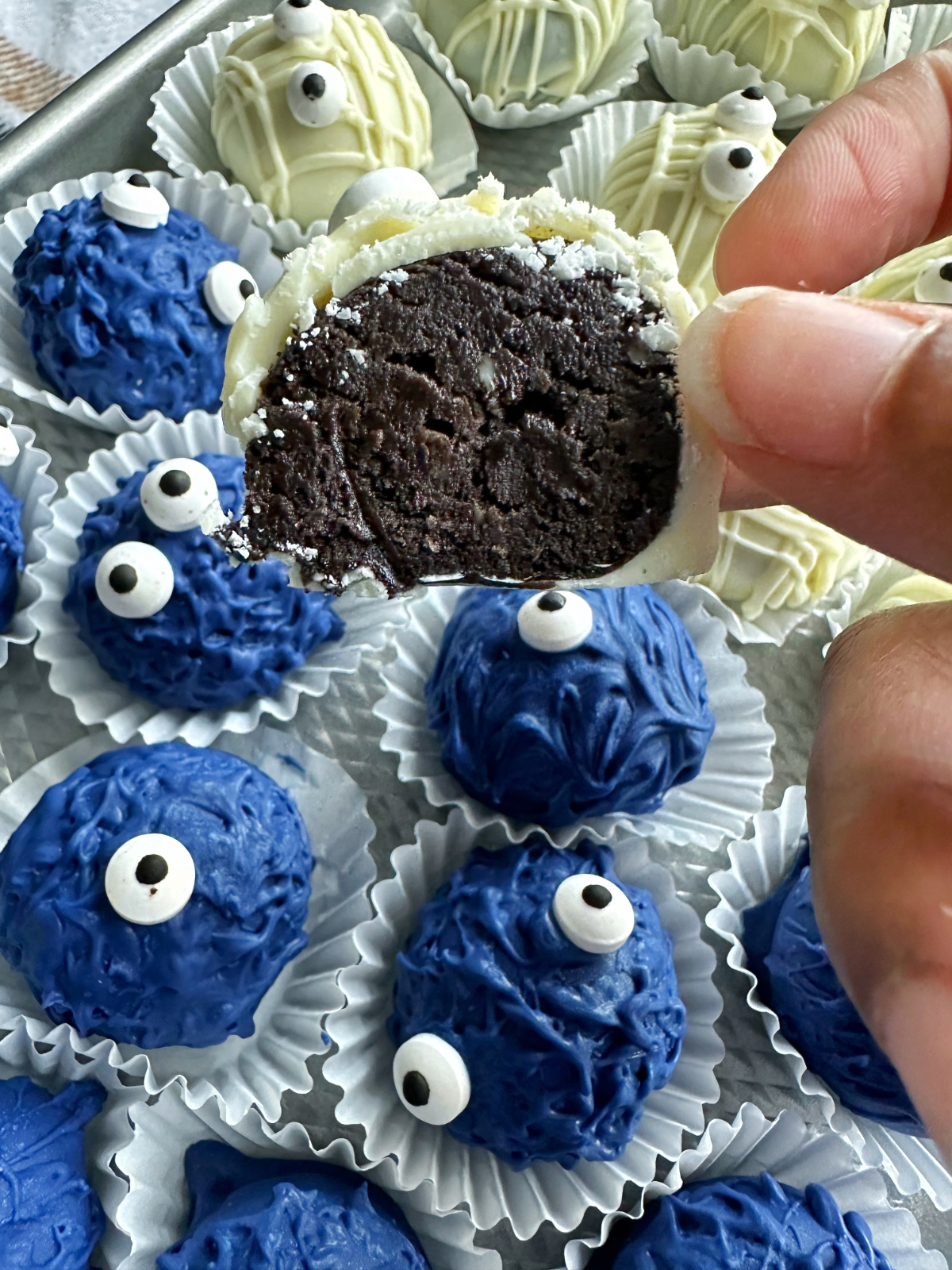 A hand holding a sliced Oreo truffle cut in half, to display the texture inside.