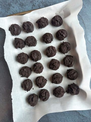 A parchment-lined pan of Oreo truffle dough, portioned out into small scoops.