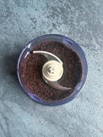 A food processor containing crushed chocolate sandwich cookies.