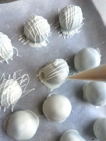 A hand drizzling white chocolate onto chocolate-dipped spheres.