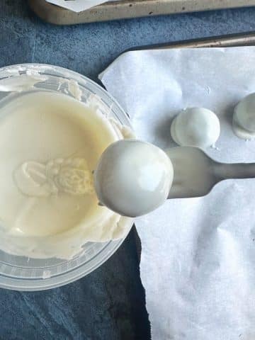 Dipping a chocolate sphere into a container of white chocolate.