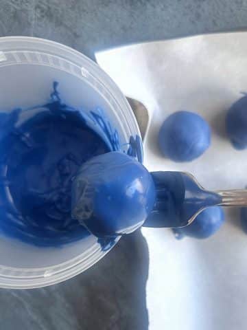 Dipping a chocolate sphere into a container of melted blue-colored candy melts.