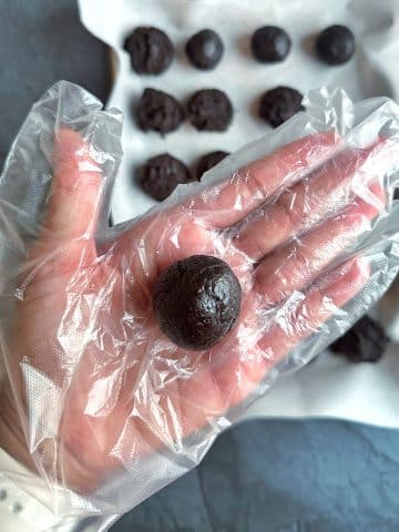 A gloved hand displaying a sphere of crushed Oreos and cream cheese.