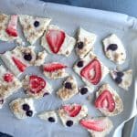Pieces of frozen yogurt bark with strawberries and blueberries on a parchment-lined pan.