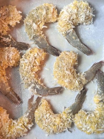A parchment-lined tray of coconut-coated shrimp before frying.