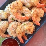 A platter of golden brown coconut shrimp with a red sauce on the side.