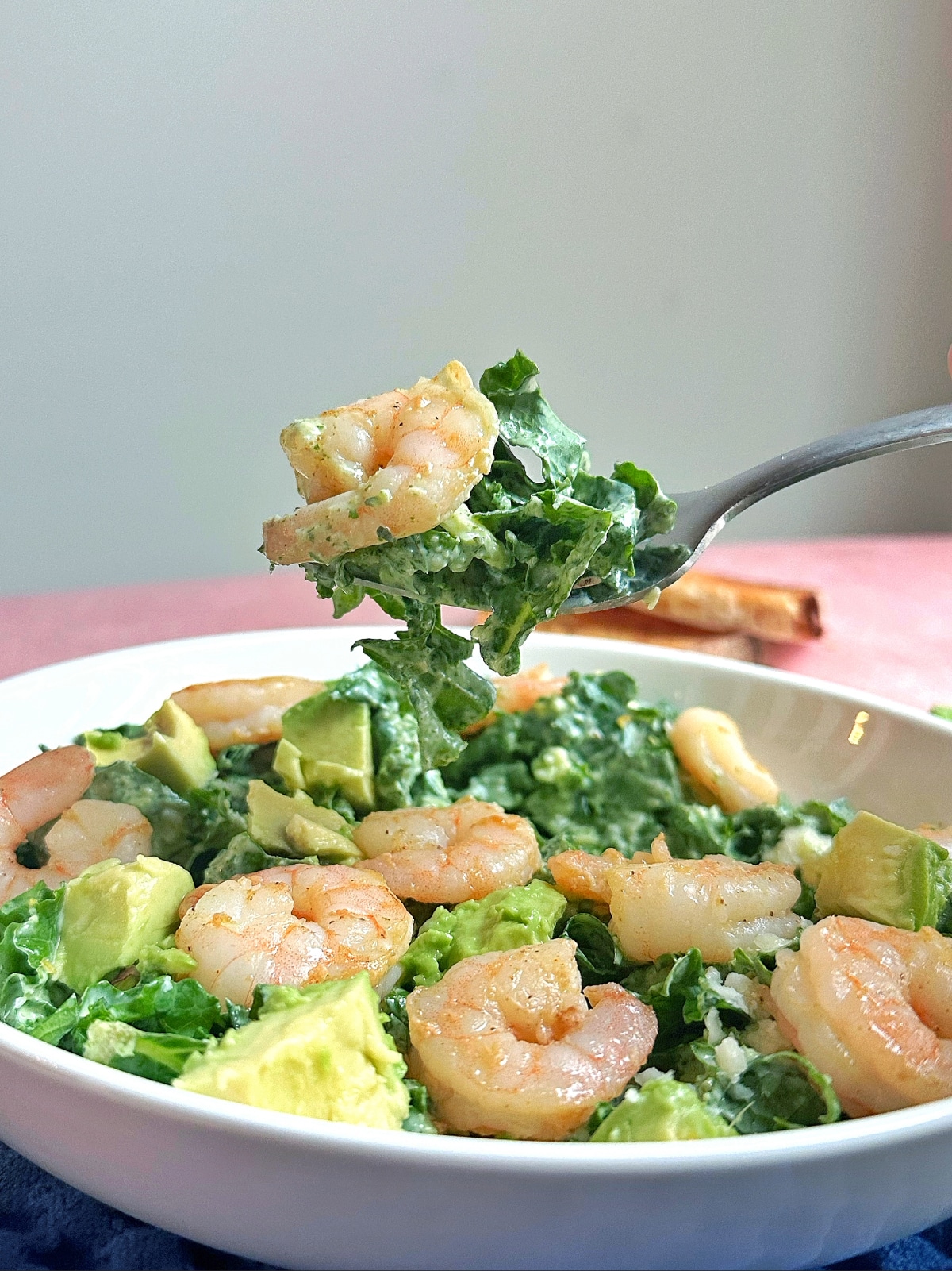 A forkful of green goddess kale salad with grilled shrimp, being held over the entire bowl.