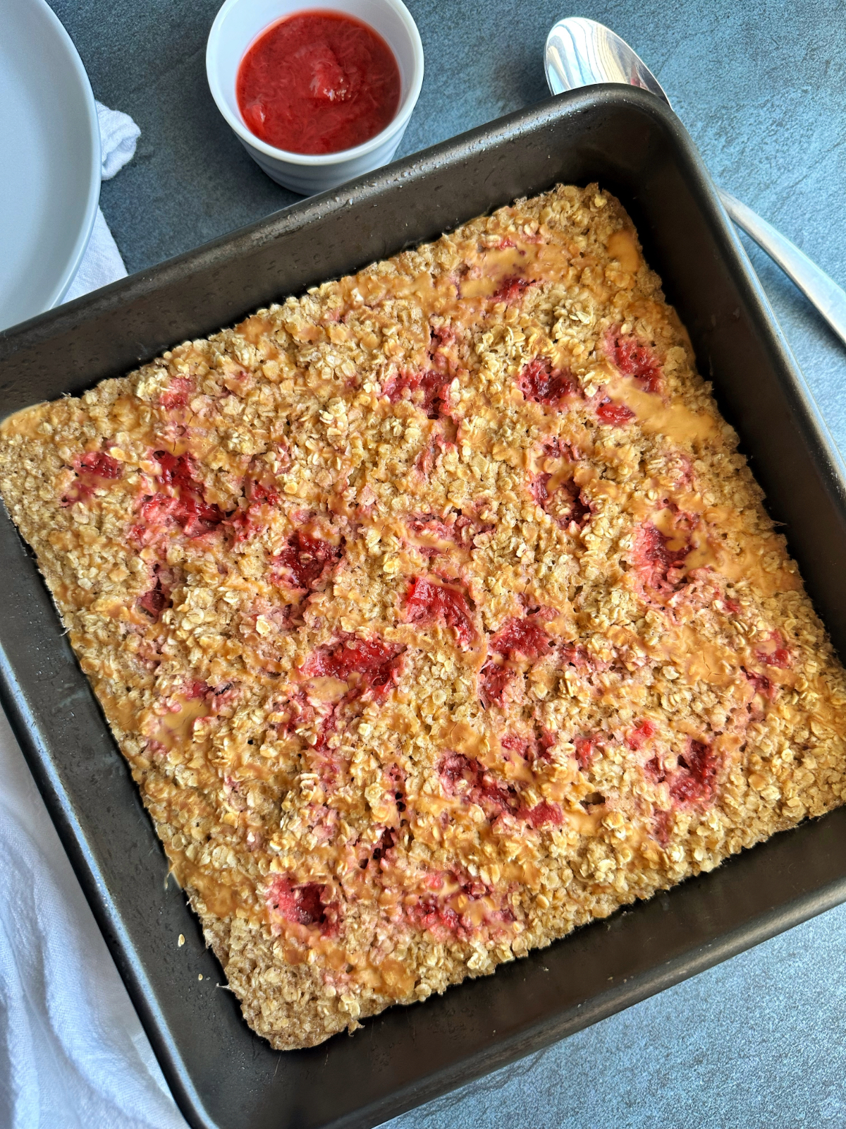 A pan containing pb&j baked oats, with a side of strawberry preserves to serve on top.