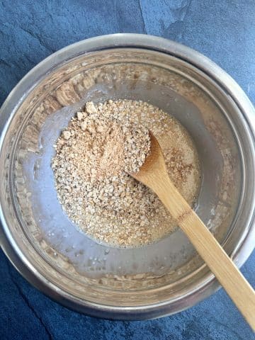 A bowl of oat milk, eggs, oats, and powdered peanut butter with a spoon sticking out of it.