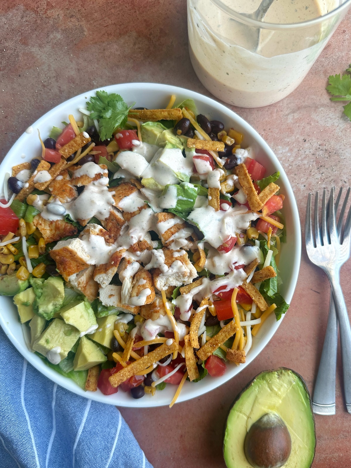 A bowl filled with chicken salad ingredients with a cup of ranch on the side.