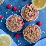 Three lemon-raspberry oat muffins on a blue board with sliced lemons and raspberries on the board.