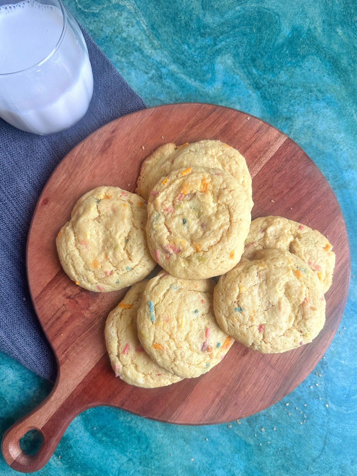 A pile of birthday cake mix cookies with a glass of milk on the side.