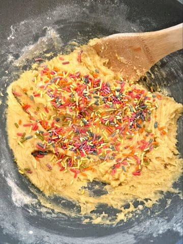A bowl of cookie dough with rainbow sprinkles poured in.
