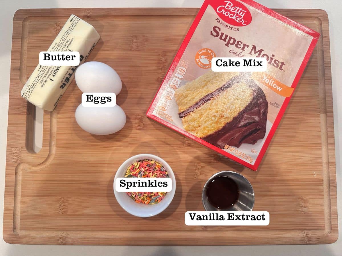 A wooden board containing ingredients for cake mix cookies, including a box of mix, butter, and eggs.