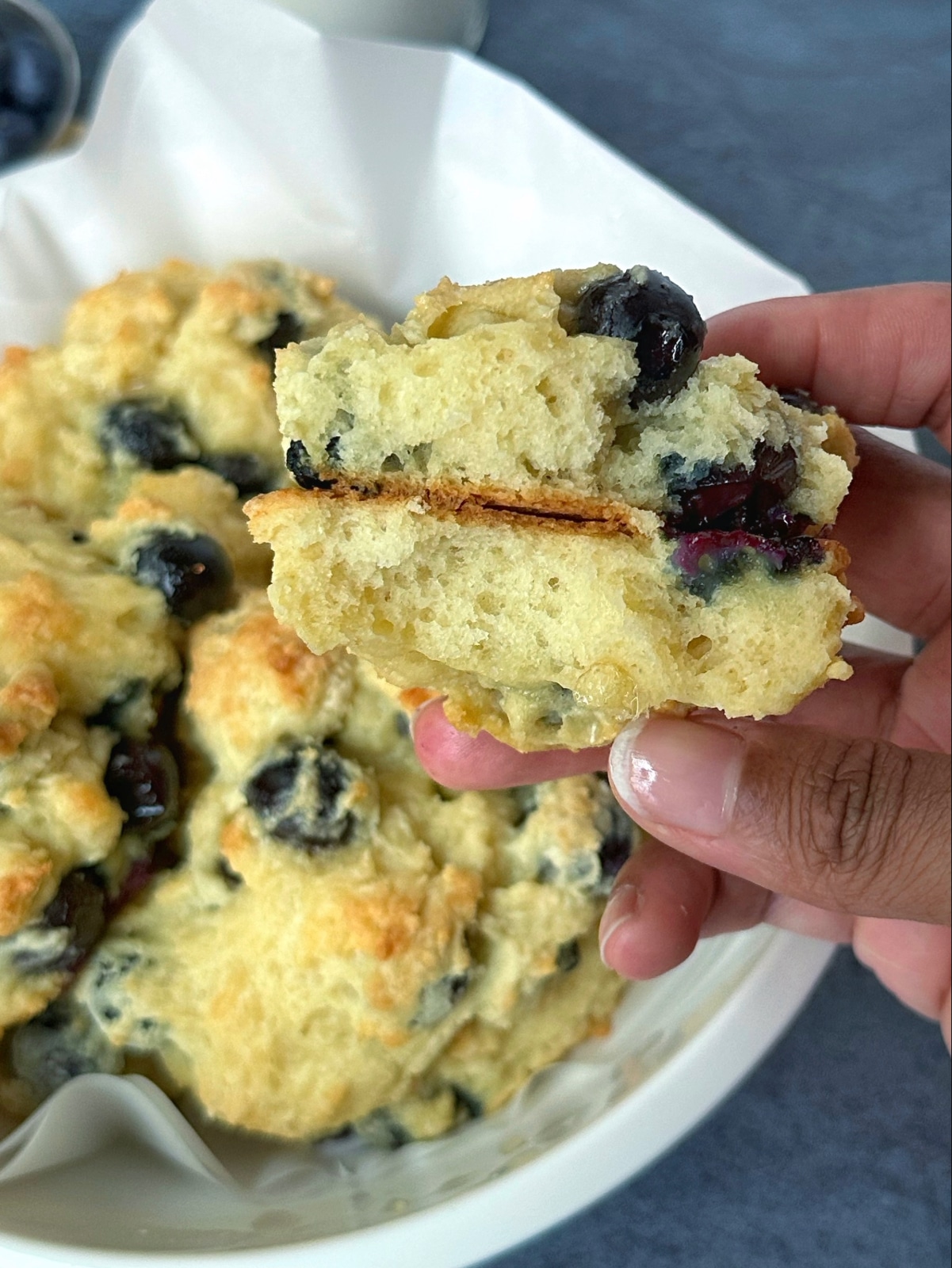 A hand holding a blueberry drop biscuit sliced in half, to show the inside texture.