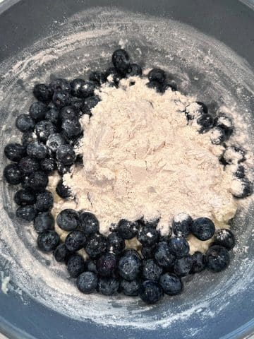 A mixing bowl filled with blueberries and flour.