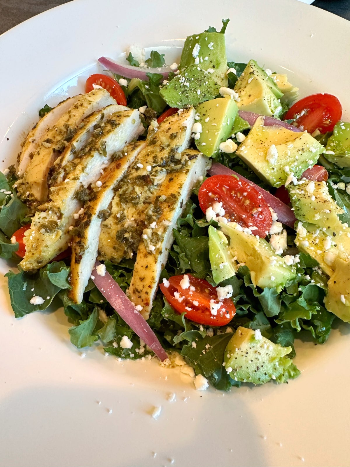 A closeup shot of a bowl of pesto chicken avocado salad.