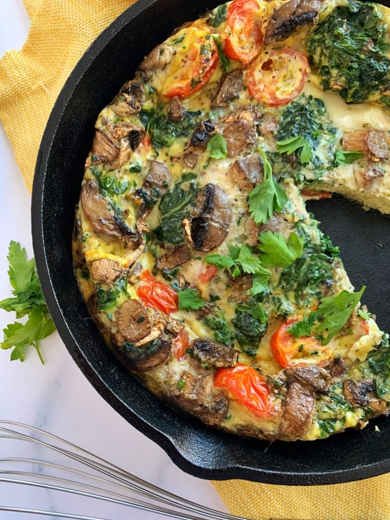 cast iron veggie frittata with a slice cut out and parsley on the side