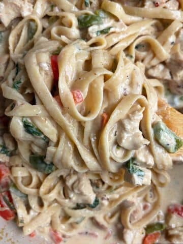 A shot of creamy jerk chicken Alfredo pasta being stirred up with a wooden serving spoon.