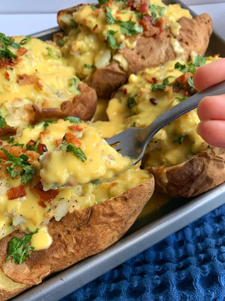 A pan of Broccoli Cheddar Loaded Stuffed Baked Potatoes with homemade cheese sauce on top.