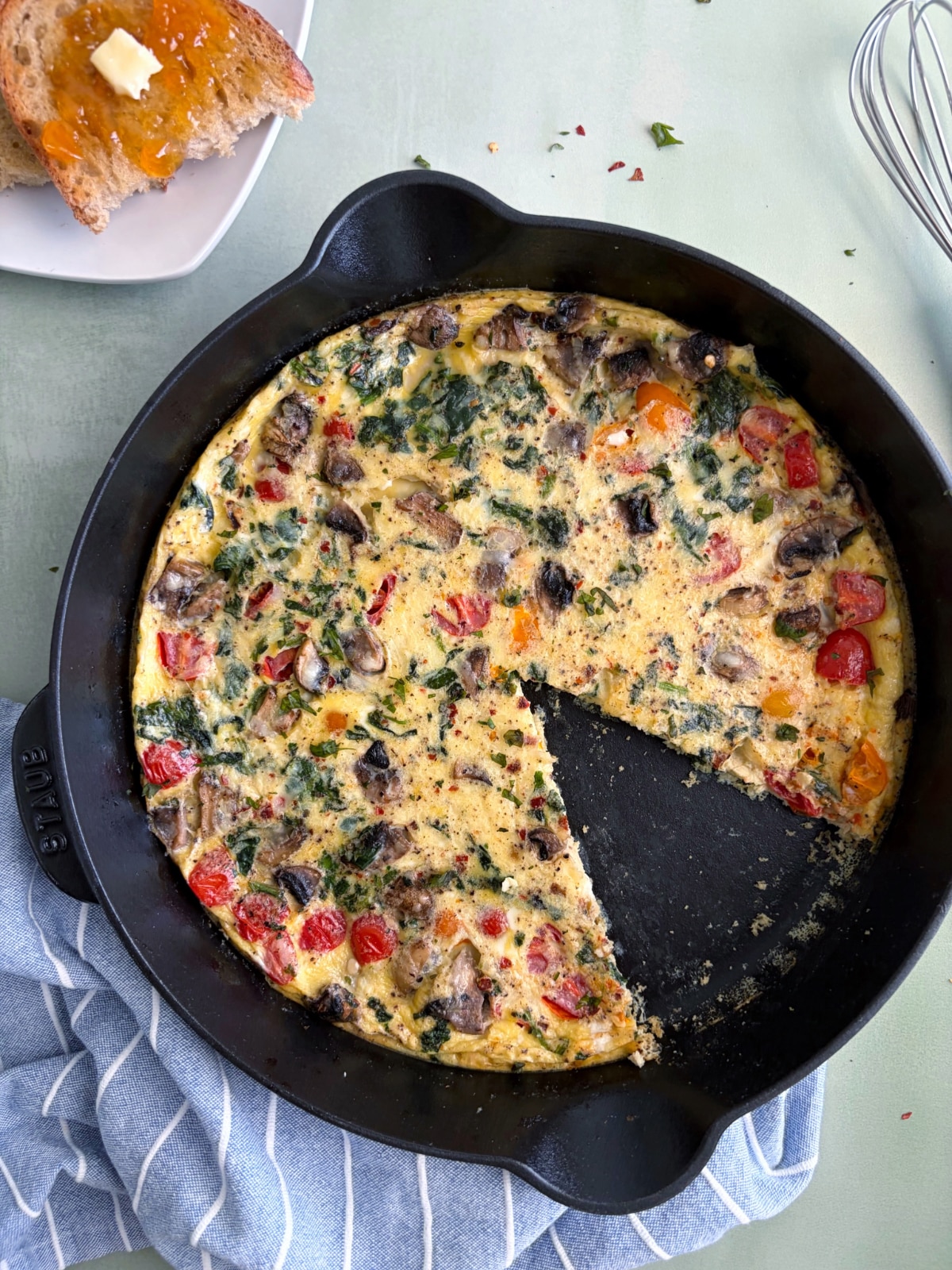 A cast iron pan with a vegetable frittata and a slice cut out of it.