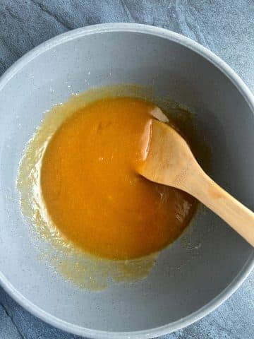 A spoon stirring a melted butter and brown sugar mixture.