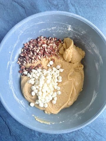 Chopped nuts and white chocolate chips poured on top of blondie batter in a grey mixing bowl.
