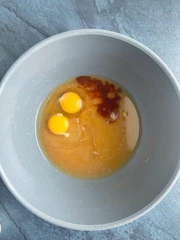 A mixing bowl containing brown sugar and butter mixed, eggs, and vanilla extract.